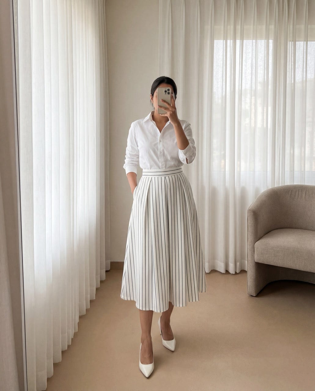 Person wearing a white shirt and black skirt in a room with curtains and a chair.